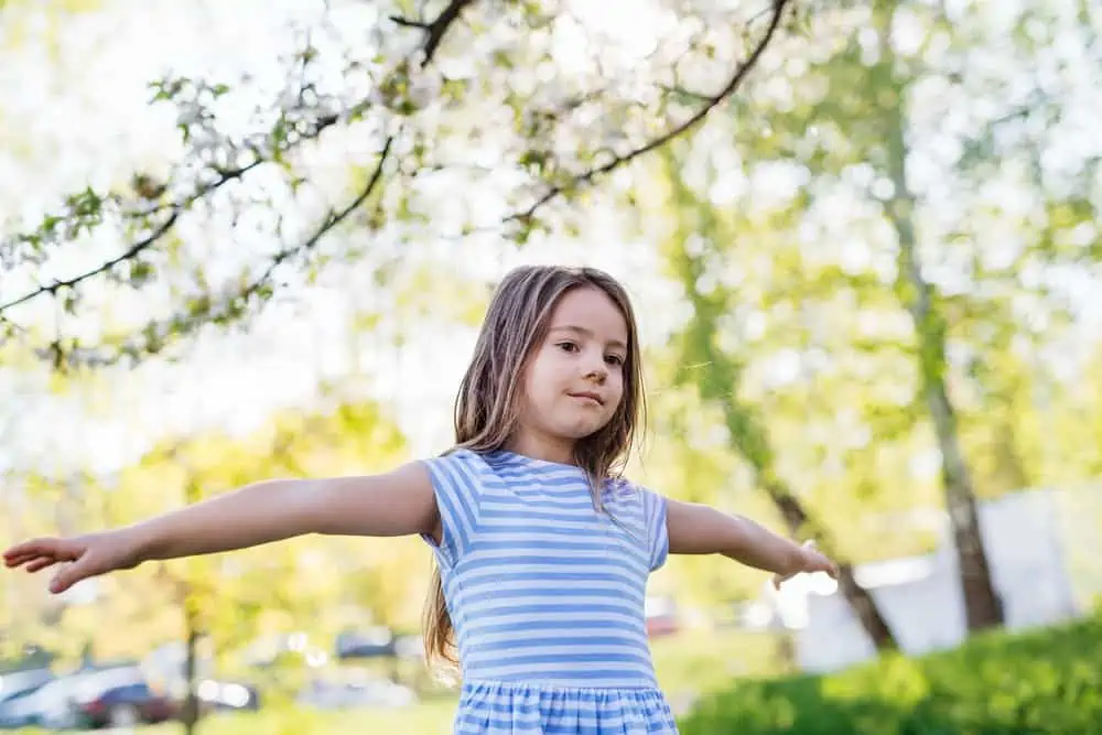 Adorable little girl standing with arms wide open in the park