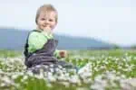 Cute little boy sitting on grass meadow with flowers