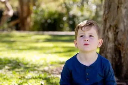 Adorable little boy sitting while looking up in the park