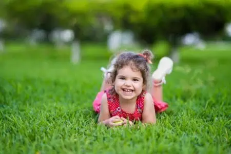 Cheerful adorable little girl laying on grass in the park