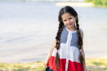 Smiling adorable little girl with long braided hair near the lake