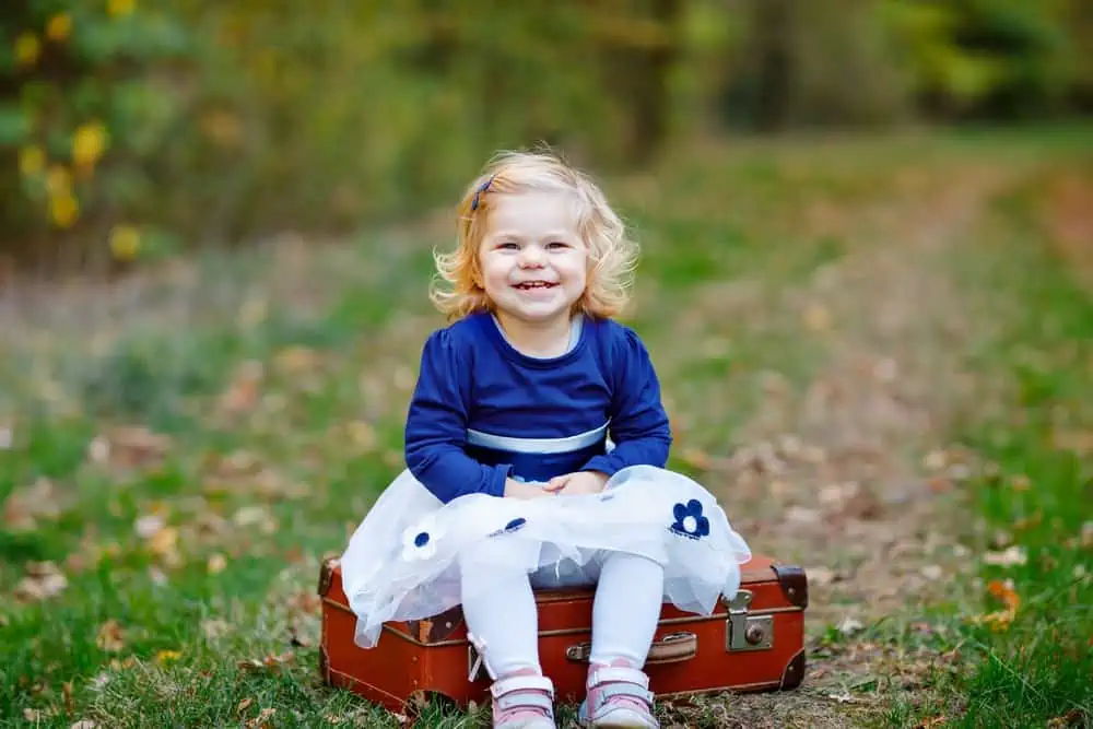 Cheerful little girl sitting on suitcase in the park