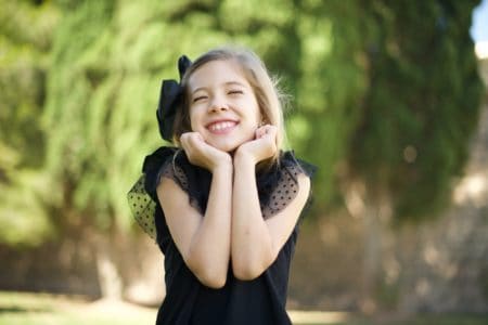 Adorable young girl posing cutely with closed eyes in the park on sunny day