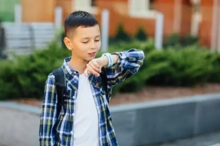 Cute young boy in plaid shirt looking at smart watch outdoors