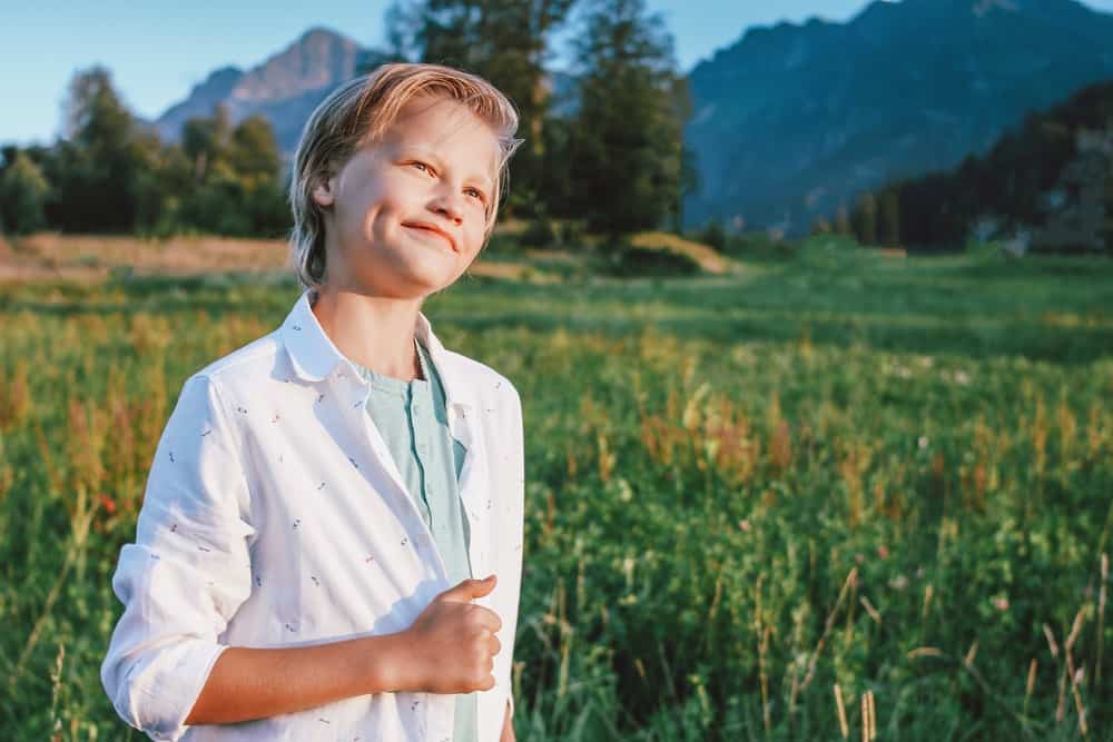 Smiling blonde boy on green meadow and mountains