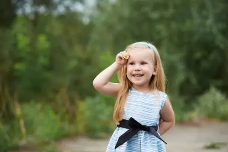 Cheerful little blond girl holding flower in the park