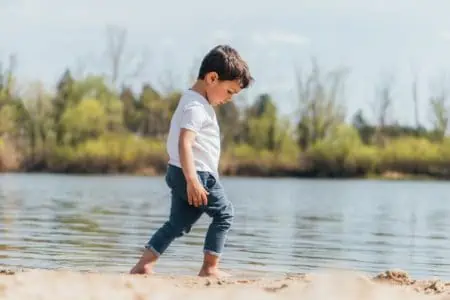 Little boy walking barefoot near lake on sunny day