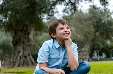 Cute little young boy sitting in the park smiling thinking about something