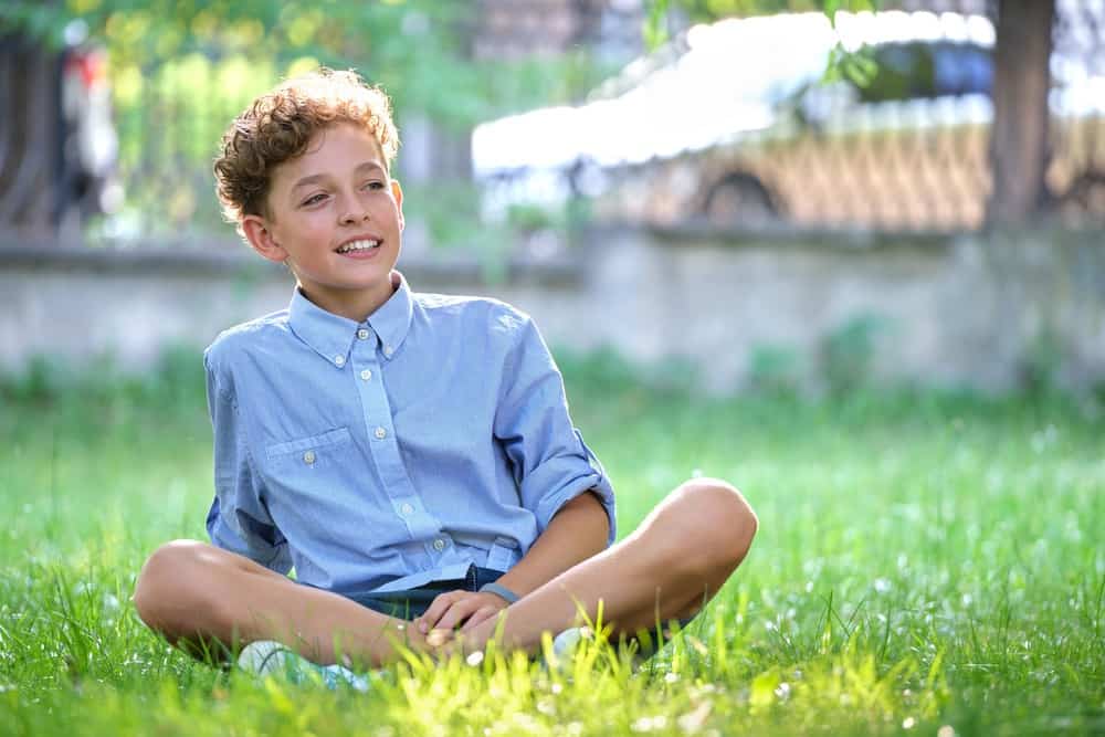 Cheerful young boy sitting on green grass in the park