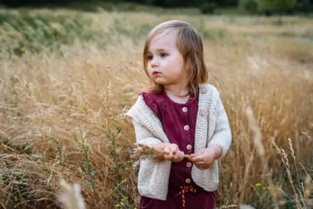 Adorable little girl in sweater holding dried grass