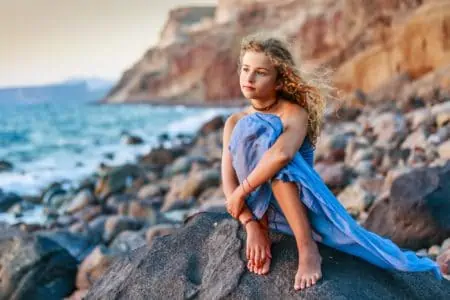 Beautiful blond curly hair girl sitting on big rocks near sea