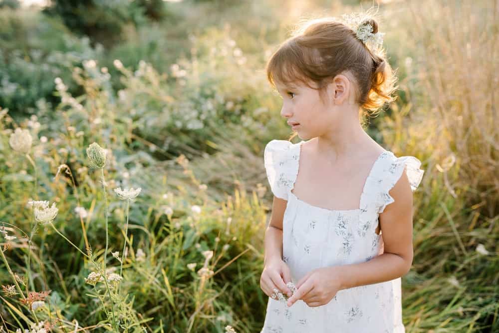 Beautiful young girl wearing white dress in flowery field on sunny day