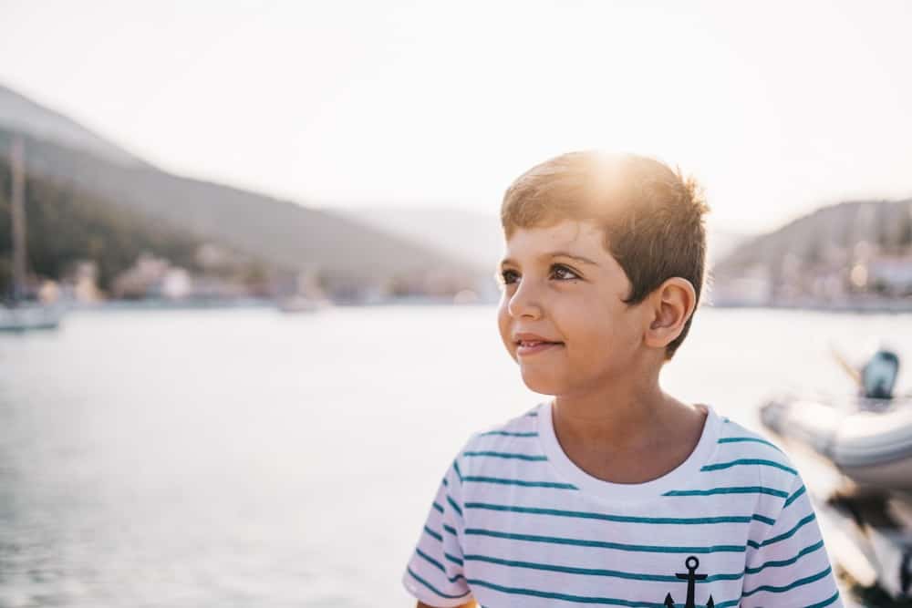 Adorable little boy smiling at sunset with sea and mountain in the background