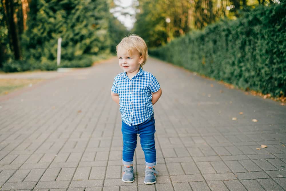 Adorable blond little boy standing in road side at the park