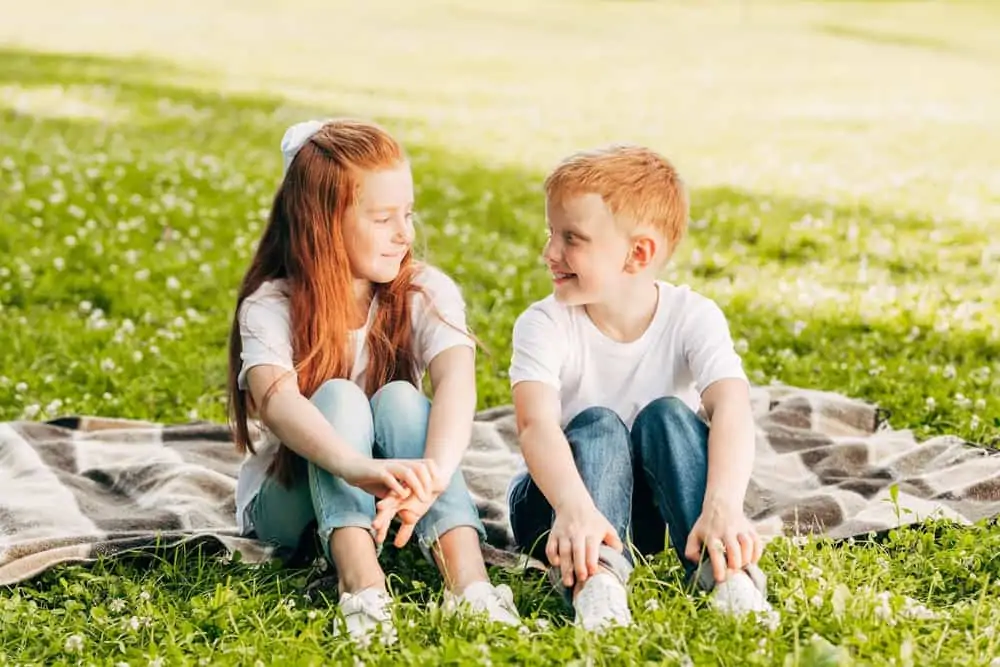 Adorable little boy and girl sitting on the grass while looking at each other