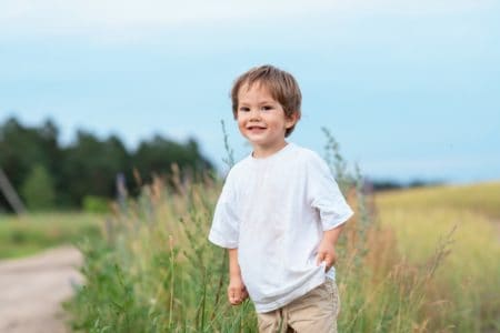 Cheerful cute little boy wearing dirty white shirt standing in meadow