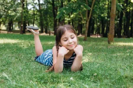 Beautiful smiling little girl lying on green grass in the park