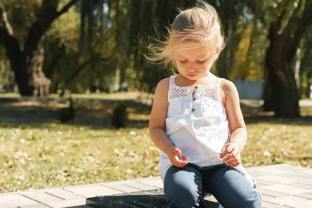 Cute little blonde girl kneeling in the park on a sunny day