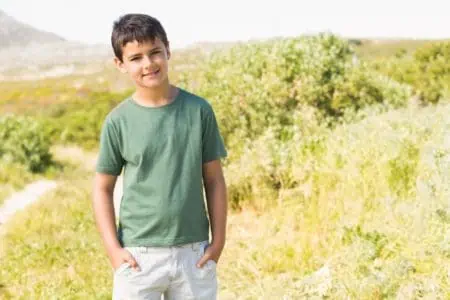 Smiling young boy standing in meadow while placing both hands in pocket