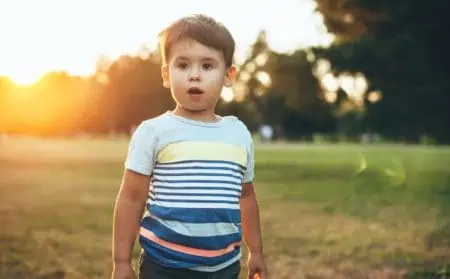 Cute little boy in casual clothes in a field with a sunset on background