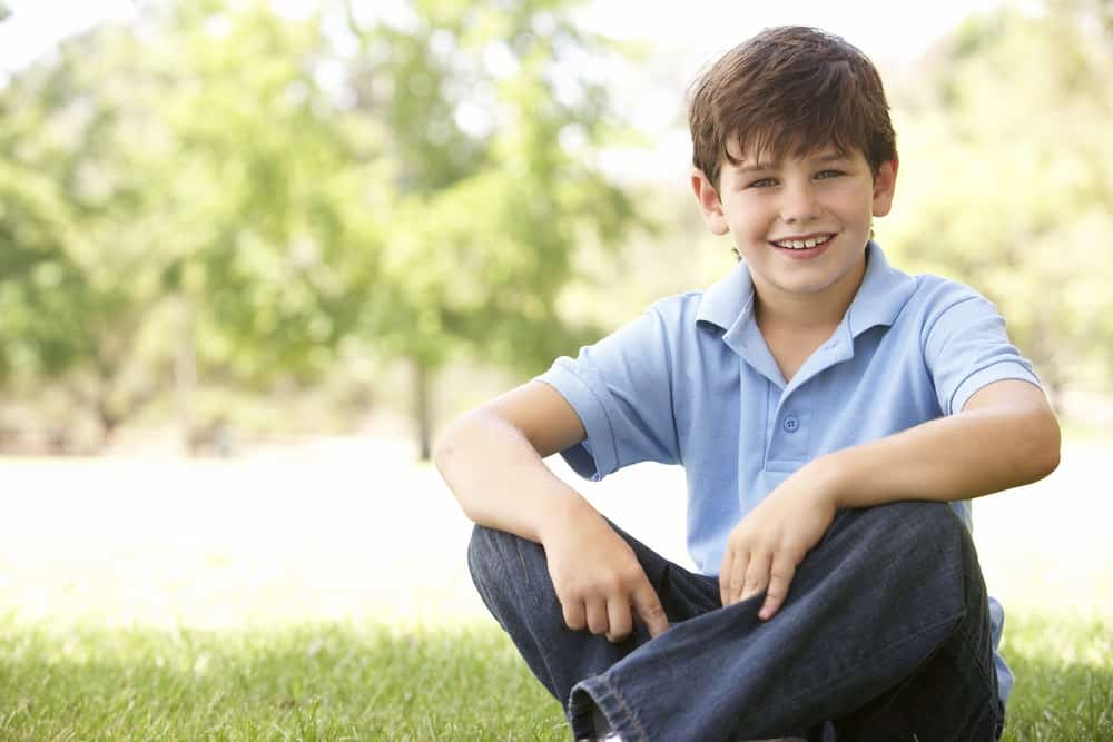 Adorable young boy sitting on the grass at the park
