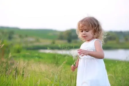 Cute little girl in green field with dandelion