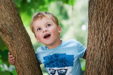 Happy little boy standing near trees in the park
