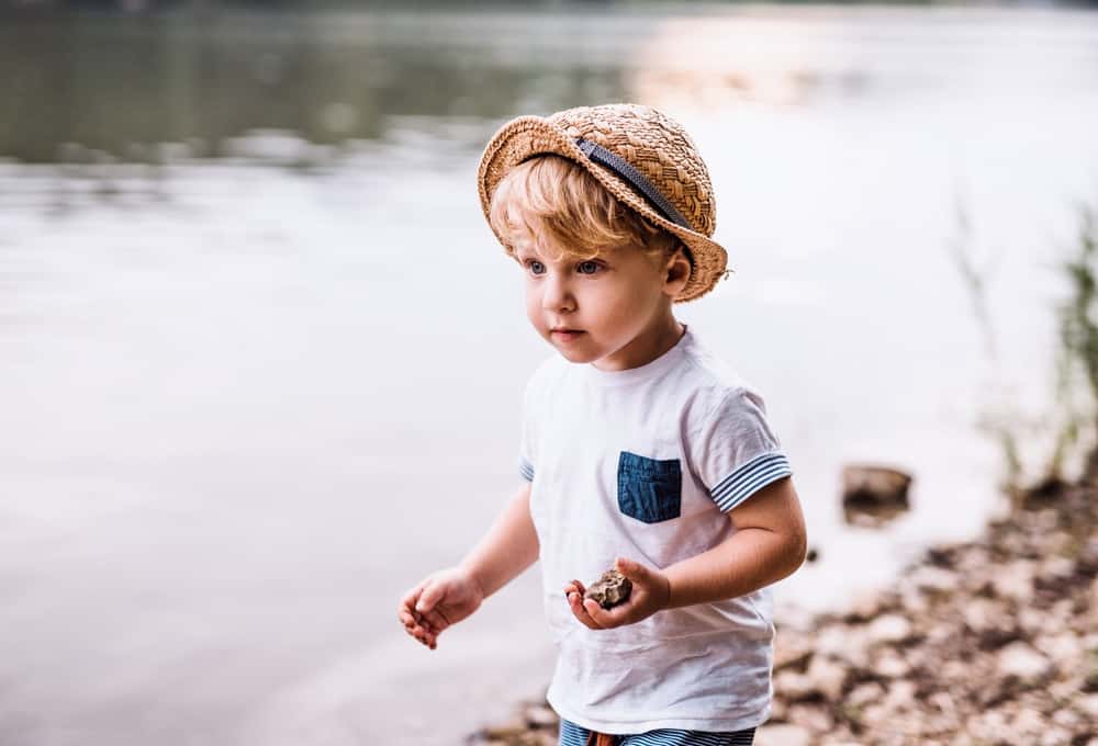 Little Finnish boy playing with rocks on the lake shore