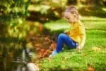 Adorable little Finnish girl sitting near brook in the park