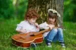 Little hippie boy and girl playing with the guitar in the park