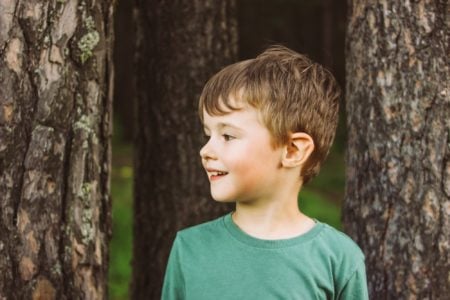 Cute little boy standing near trees in the park