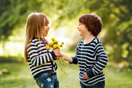 Happy little boy giving a bouquet of dandelions to a girl in the park