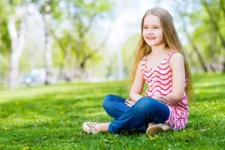 Smiling little girl sitting on the grass in the park