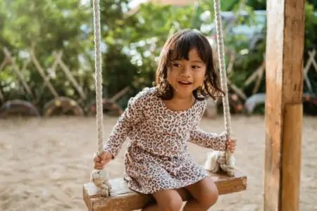 Happy little Thai girl sitting on the playground swings