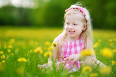 Adorable little girl sitting in the blooming dandelion meadow