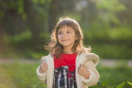 Adorable young girl wearing jacket smiling brightly during sunset in the park