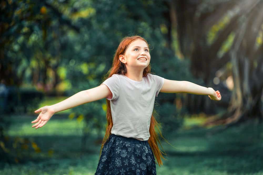 Cheerful girl looking up with arms wide open playing at the park