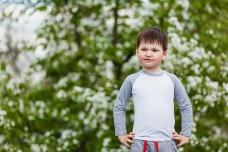 Cute little young boy standing with both hands placed on his waist on sunny day at the park