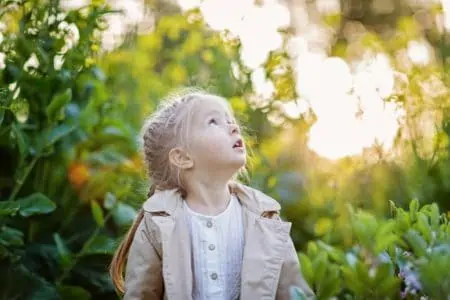 Beautiful little girl looking up with blooming yellow flowers in the background