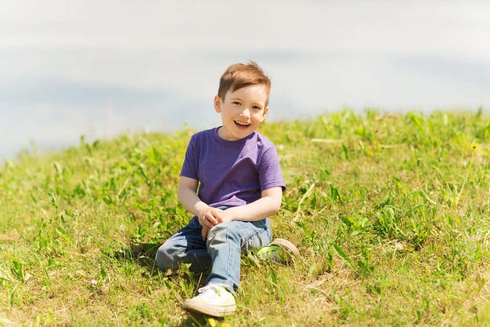 Happy little boy sitting on grass outdoors on sunny day