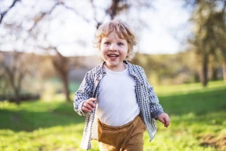 Cheerful toddler boy running outside in spring nature