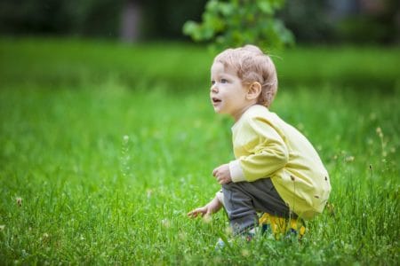 Cute blonde little boy sitting and touching the grass