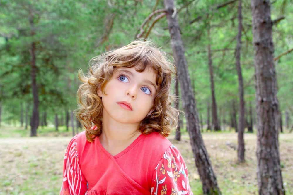 Curly-haired beautiful girl in forest nature trees thinking gesture