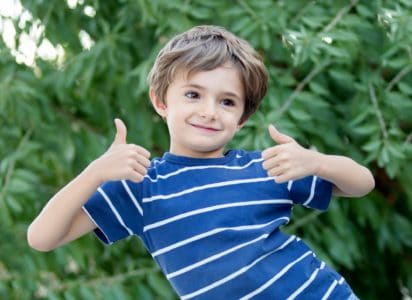 Cheerful boy posing with thumbs up in nature background