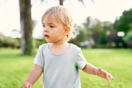 Adorable toddle girl walking on green lawn at the park