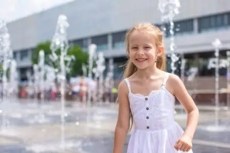 Cheerful girl in white dress having fun in street fountain