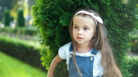Pretty child girl standing outdoors in green summer park