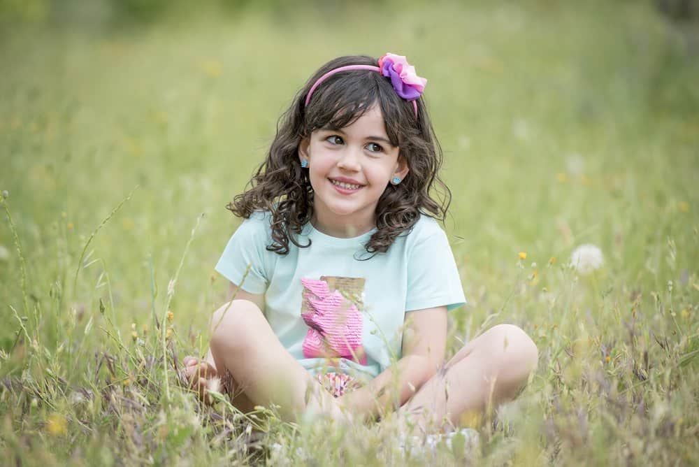 Cheerful young girl posing for the camera while sitting on the grass in green meadow