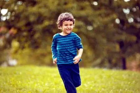 Curly-haired adorable young boy running at the park