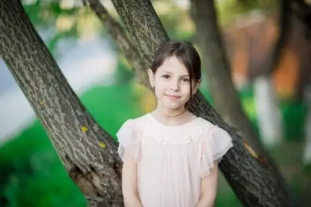 Adorable young girl standing near the trees in the park